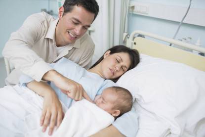 padre assiste la compagna che dorme ed il figlio appena nato