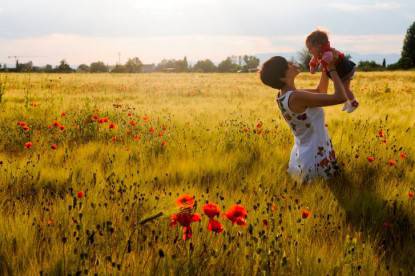 Woman smiling in a poppy field with her babby girl.