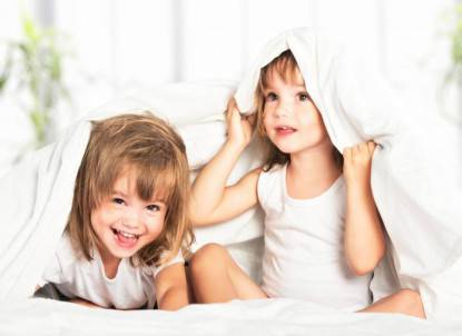 happy little girls twins sister in bed under blanket having