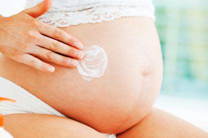 Young pregnant woman applying moisturizer on her belly.