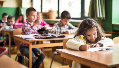 Elementary student studying in classroom. There are people in the background.