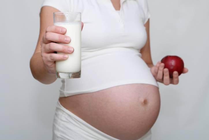 Donna incinta con bicchiere di latte e mela in mano