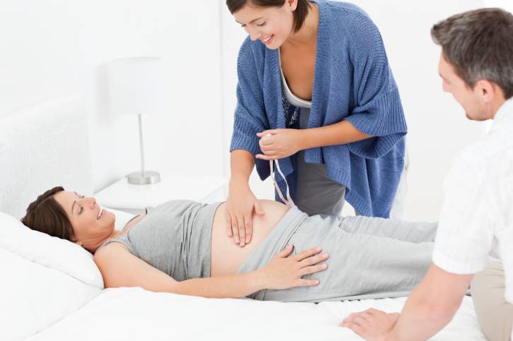 Ostetrica che controlla la donna incinta con il marito presente