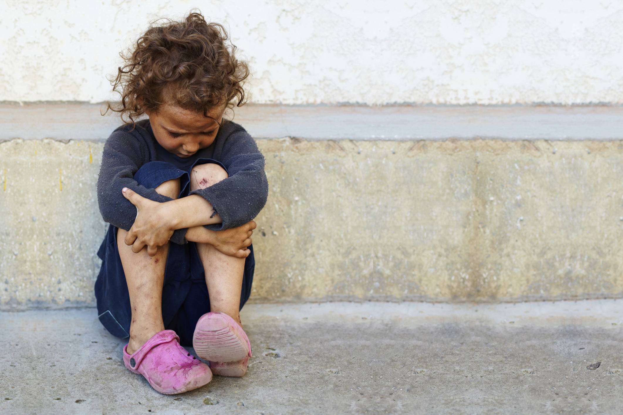 Bambina povera appoggiata su un muro