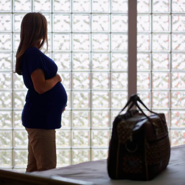 Donna incinta in ospedale e valigia in primo piano