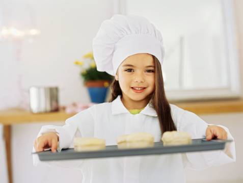 Bambina vestita da chef mentre porta un vassoio con dolci
