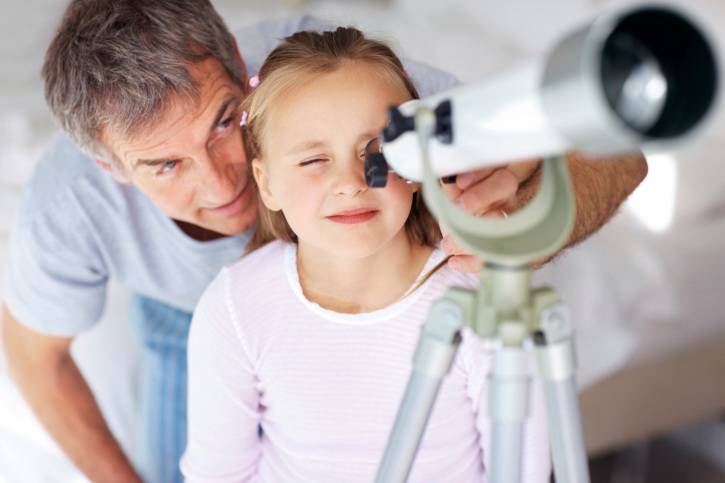 Bambina con papà accanto guarda il cielo con il telescopio