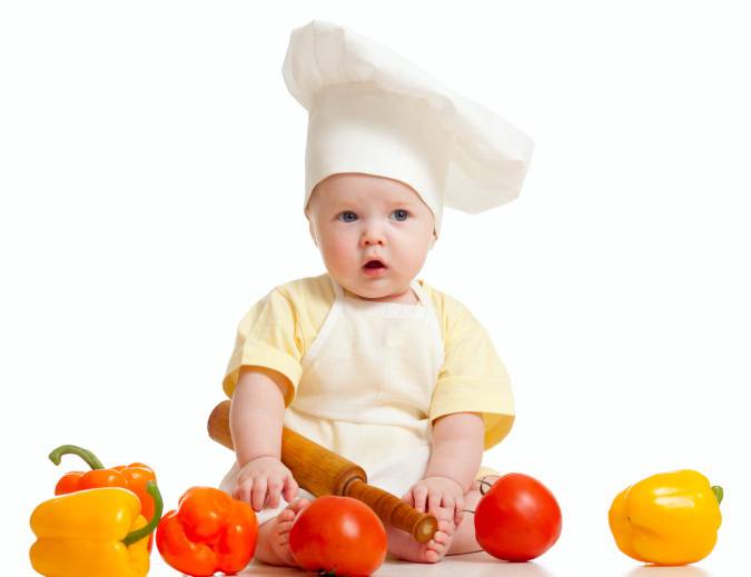 Bambino vestito da chef con verdura e frutta intorno