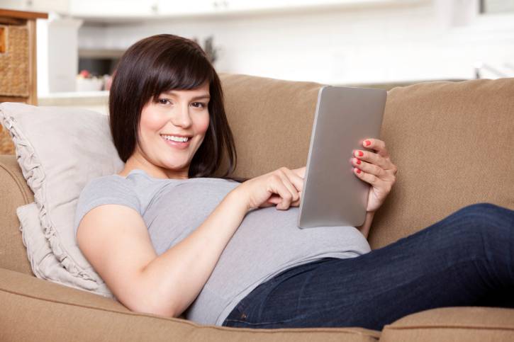 Donna incinta sul divano mentre digita su un tablet