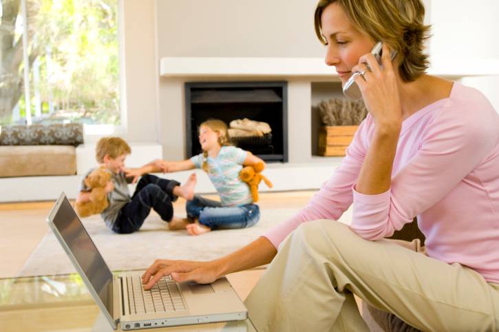 donna che parla al telefono,e usa il pc. sullo sfondo dei bambini che giocano