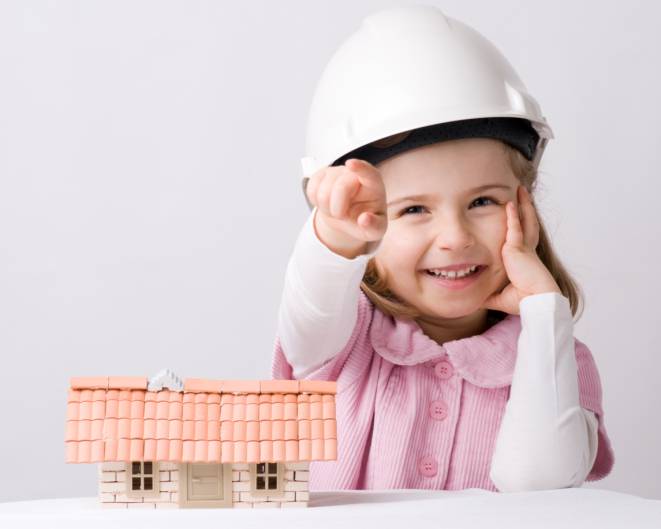 Bambina che indossa un caschetto di protezione di fronte a un modellino di casa