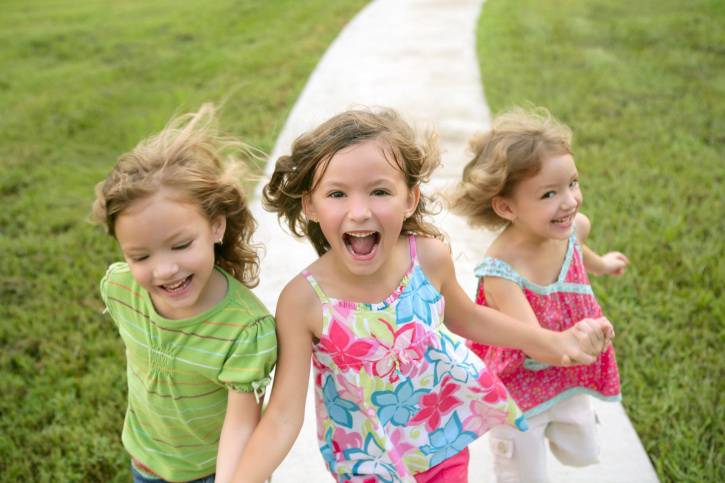 Tre bambine corrono sul prato felici.