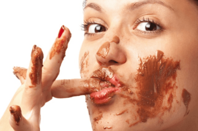 Ragazza col viso spocrco di cioccolato si lecca le dita