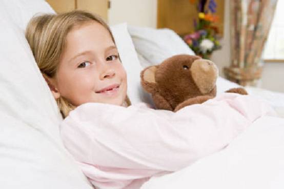 bambina in letto d'ospedale con orsacchiotto