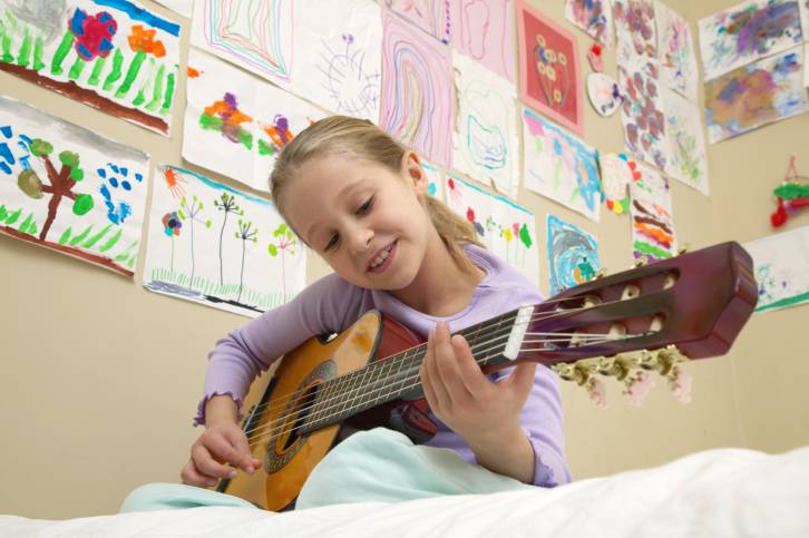 bambina che suona la chitarra sul letto