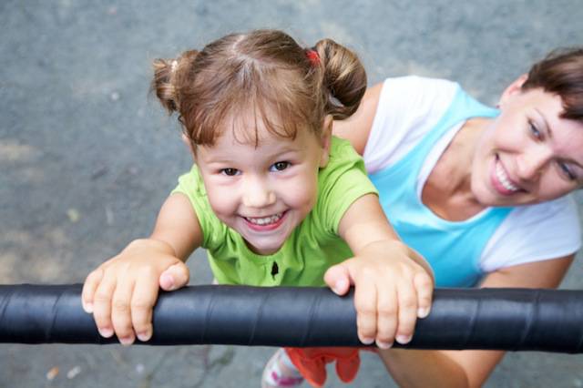 Una bambina viene sorretta dalla mamma mentre è appesa ad un gioco