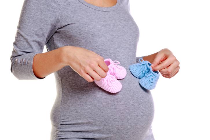 Una donna incinta sta tenendo due scarpine da bambino: una rosa e l'altra azzurra.