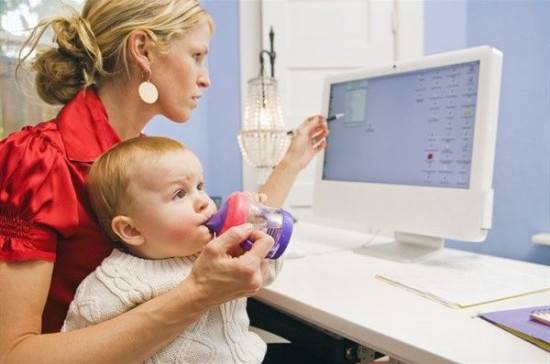 donna che lavora al computer che tiene sulle ginocchia un bambino a cui tiene il biberon