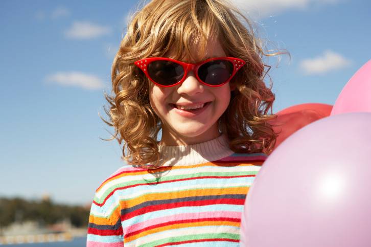 bambina sorridente che tiene in mano un pallone e indossa occhiali da sole