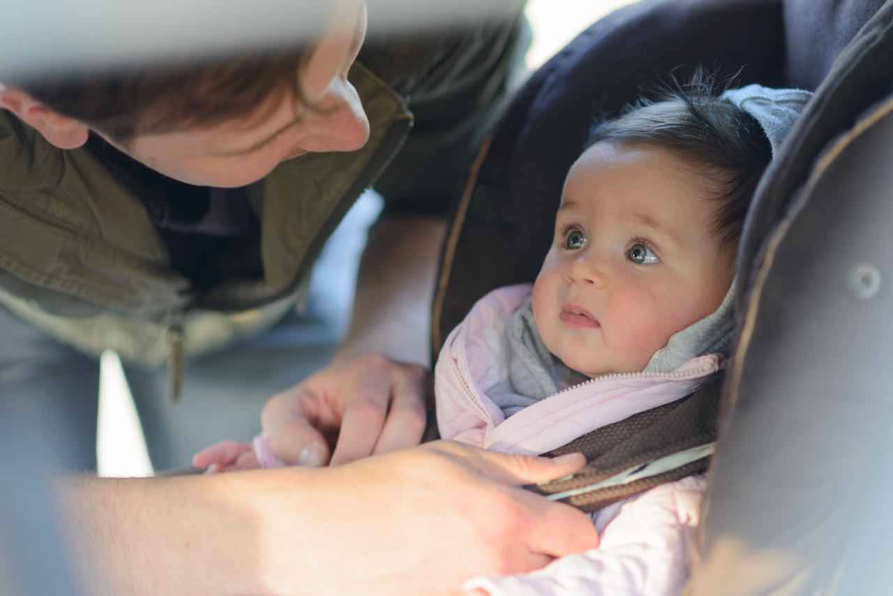 papà lega bambina al seggiolino in auto