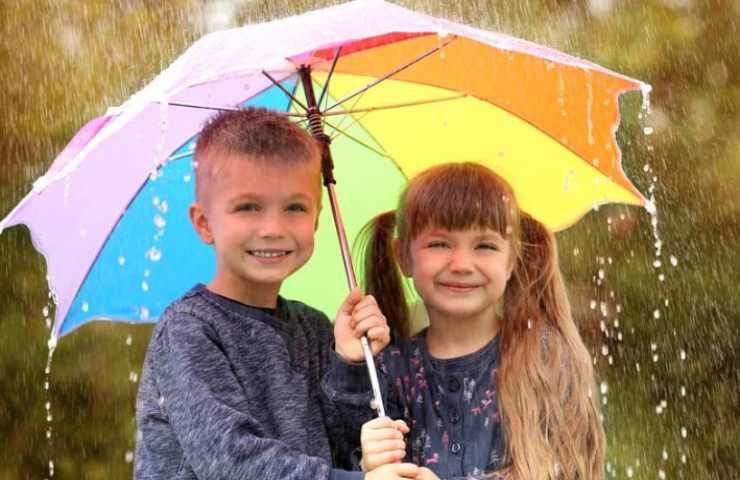 Bambini sorridenti con l'ombrello sotto la pioggia